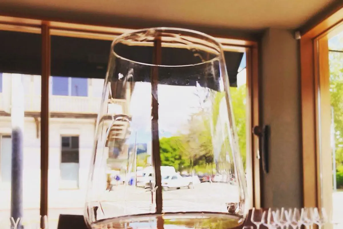 Copa de vi rosat de color salmó pàl·lid sobre una taula de fusta, amb una ampolla desenfocada al fons